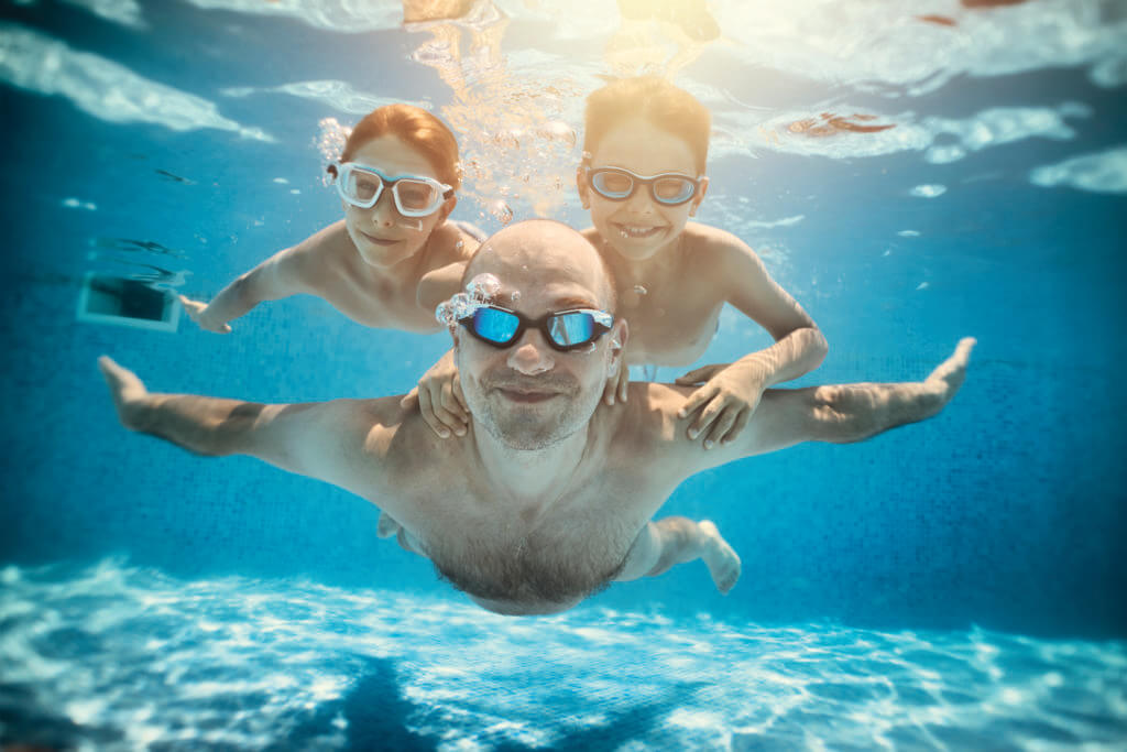 Father and sons playing underwater in resort pool. Family is playing underwater superheroes.