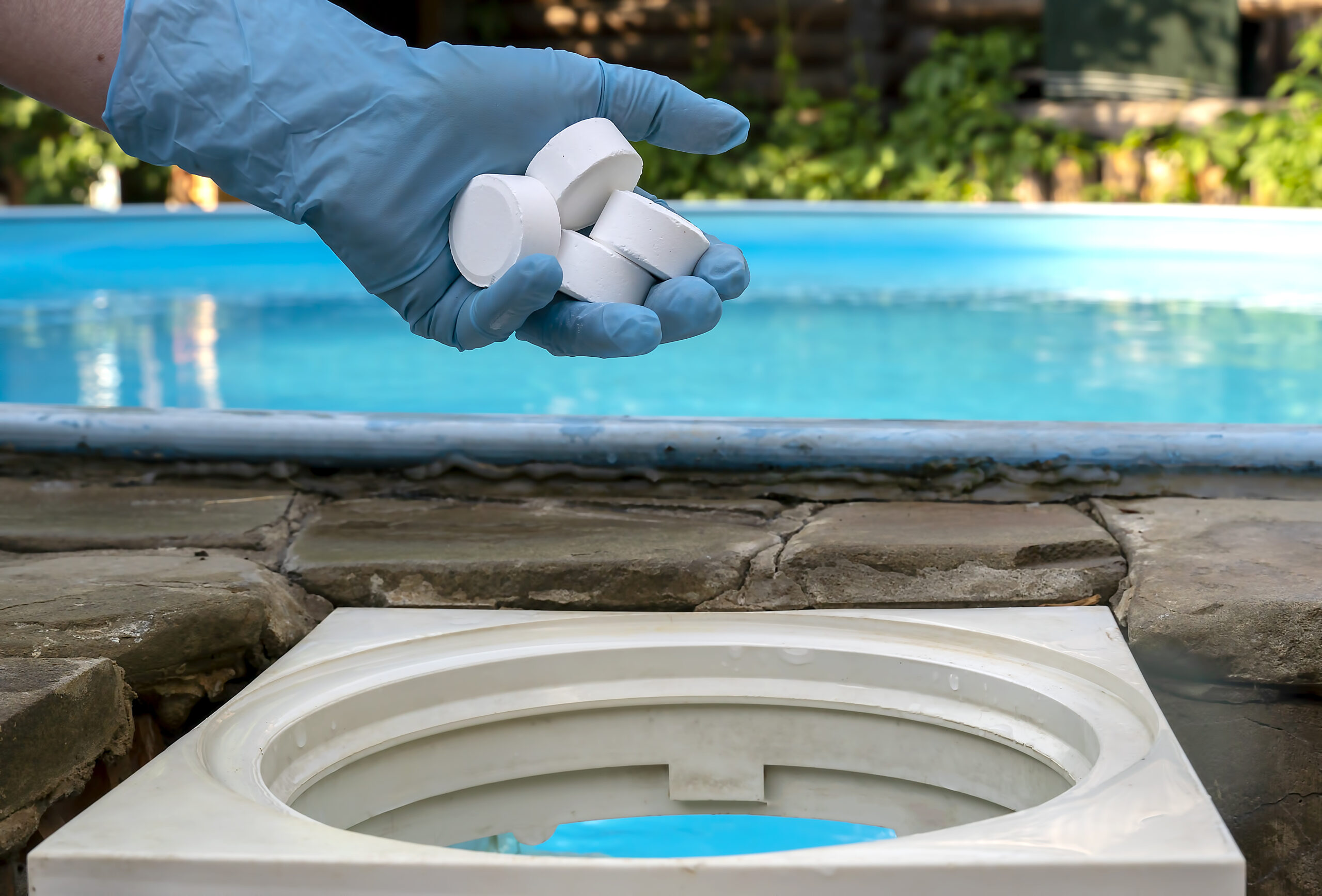 Female hand puts white tablets into pool skimmer. Cleaning, disi Female hand puts white tablets into pool skimmer. Cleaning, disinfection of water in the swimming pool.