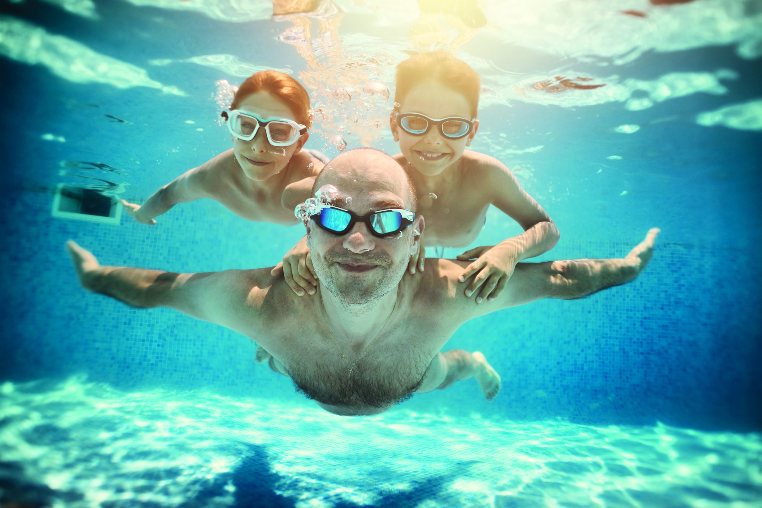 Father and sons playing underwater in resort pool. Family is playing underwater superheroes.