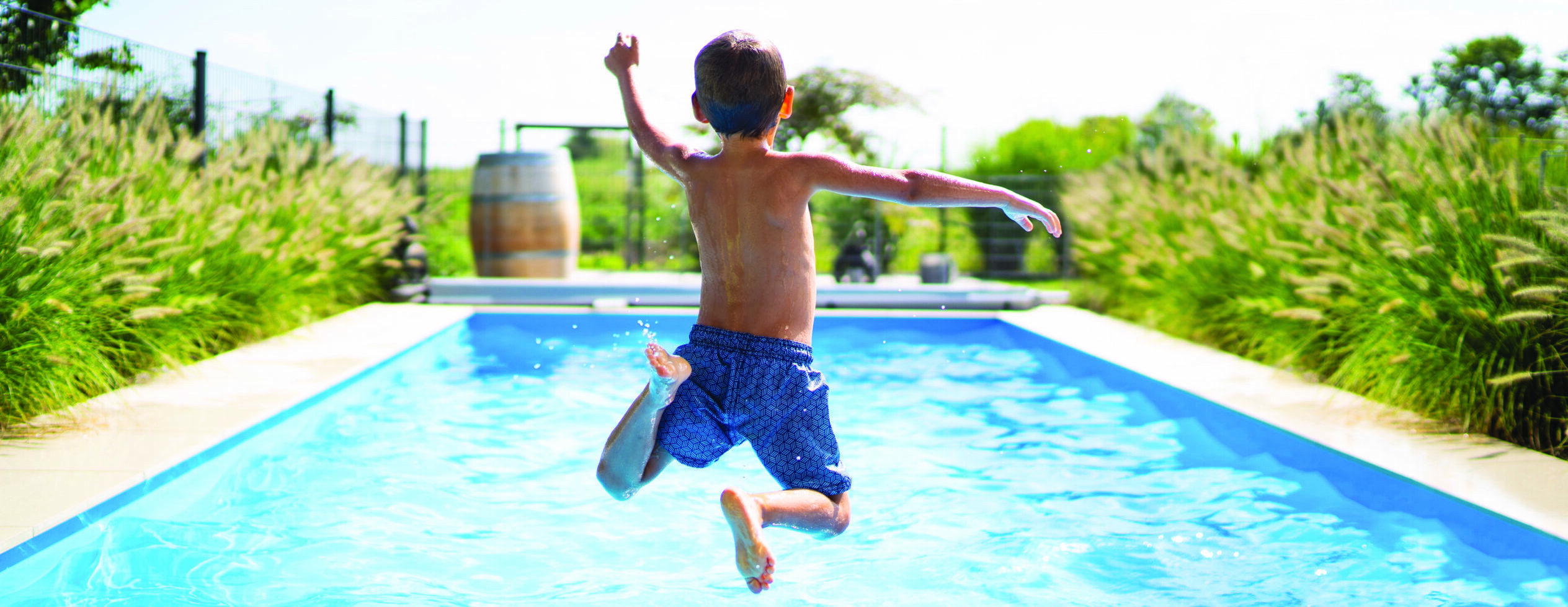 rear view of 4 year old boy jumping into private pool on sunny vacation day - boy is unrecognizable so can be used anonymous summer fun series